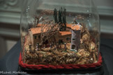 <center>Exposition de crèches en 2017.</center>Lucie André Datation inconnue Crèche sous un dôme en 34 x 29 x 29. <br>
LES CRÈCHES PROVENÇALES
La crèche apparaît en Provence du XVIIe siècle à la faveur de l'activité de la confrérie religieuse de l’Oratoire. Durant le XVIIIe siècle, les crèches viennent investir quelques églises de la région, cette pratique restant cependant peu répandue.
En parallèle des crèches d'églises, les crèches domestiques font leur apparition. On attribue parfois leur multiplication au contexte du lendemain de la Révolution française. En effet, cette époque est marquée par une suspension du culte et la fermeture des églises. Les parparoissiens auraient alors pris, pour certains, l'initiative de construire de petites crèches chez eux, dans un contexte de mutation des attitudes à l'égard de l'enfance. Les enfants imitent en effet les cérémonies religieuses et jouent « à la chapelle » en utilisant des santouns, au départ petites statuettes de bois ou de plâtre. Cette tradition enfantine est à l'origine de l'apparition des santons, ou « petits saints », personnages d'argile peint qui peuplent les crèches provençales. La création du santon d'argile a été attribuée au marseillais Jean-Louis Lagnel (1764 - 1822), qui se dit sculpteur et qui a son atelier entre Saint-Laurent et les Accoules. Mais c'est au XIXe siècle que la crèche apparaît réellement à Marseille dans les formes que nous lui connaissons traditionnellement aujourd'hui.
