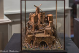 Henri Valentini 1946
Crèche en liège, moulin mécanique, santons-puces 29,5 x 26 x 23,5 cm. <br>
« L’idéal de la miniaturisation poussée à l’extrême a fait naître l’œuvre étonnante de Paul Pontet (Marseille 1987), qui fut représentant de commerce mais était fils d'un horloger et tenait sans doute de son père l’habitude du travail avec la loupe d’œil. P. Pontet réalisa tour à tour une crèche dans une ampoule de verre, une coquille d'escargot (40 santons de 1 à 5 mm), une demi-coque de noix, un dé à coudre (dix-huit santons, deux maisons, un moulin). Il plaça enfin vingt santons de 1,5 à 2.5 mm sur un demi-pépin de mandarine Il aurait également rassemblé des santons sur un grain de riz et une lentille » Régis Bertrand.